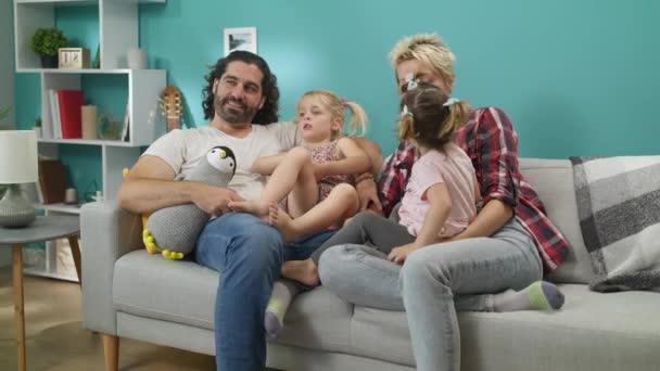 Счастливая семья смотрит смешные мультфильмы, сидя дома на диване — стоковое видео