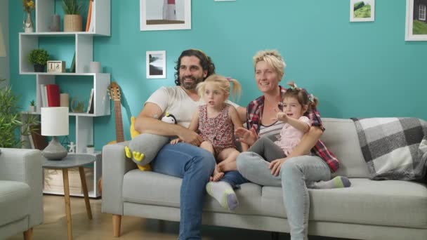 Madre, padre, hijas sentadas en el sofá en casa y viendo dibujos animados divertidos — Vídeo de stock