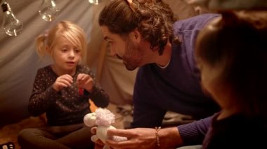 Kızları olan baba evde bir çadırda oyuncak tek boynuzlu at ile oynuyor.