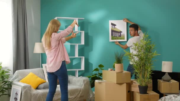 Молодая пара вешает настенные росписи в новой квартире — стоковое видео