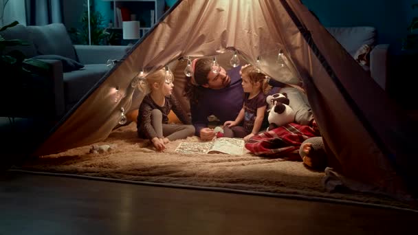 Heureux père de famille et petites filles lire un livre dans une tente à la maison — Video