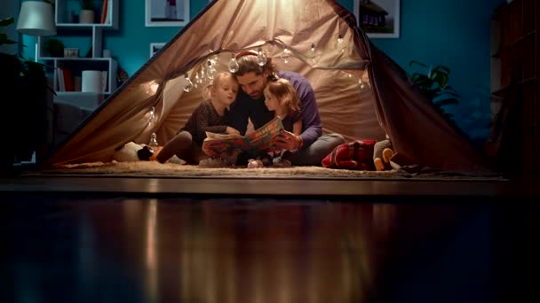 행복한 아빠와 작은 딸은 거실에서 텐트에서 책을 읽습니다. — 비디오