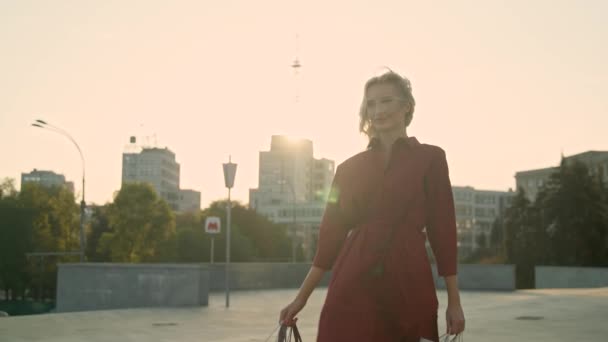Mujer con bolsas de compras caminando en una ciudad al atardecer. Movimiento lento — Vídeo de stock