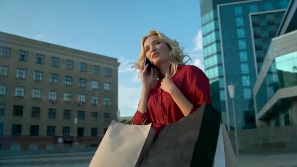 Jeune femme en robe rouge appelle au téléphone après avoir fait du shopping dans une boutique — Video