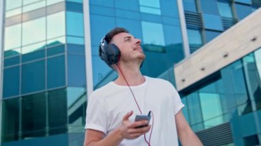 Genç bir adam kulaklıkla müzik dinler ve şehirde yürür.