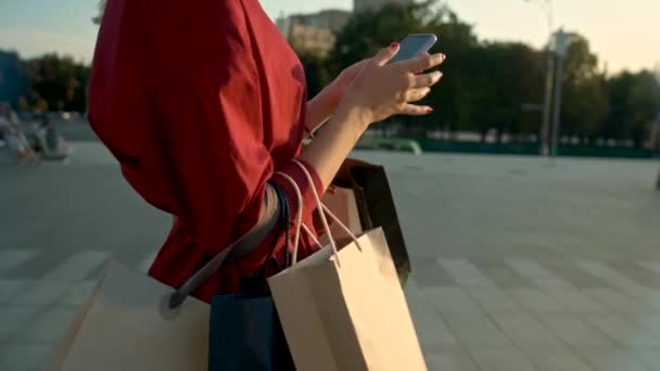 Νέα γυναίκα με ένα κόκκινο φόρεμα χρησιμοποιεί το τηλέφωνο μετά από τα ψώνια σε μια μπουτίκ — Αρχείο Βίντεο