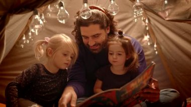 Baba ve kızları oturma odasında el yapımı bir kulübede kitap okuyor.