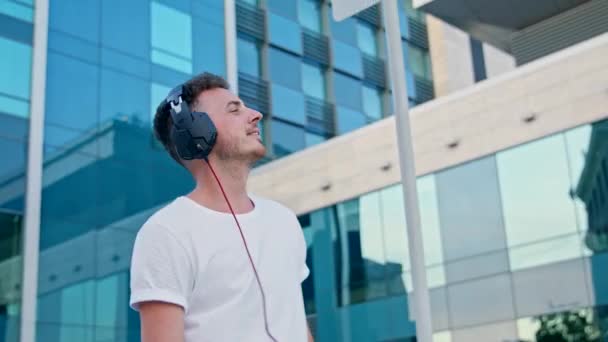 Ένας νεαρός άνθρωπος ακούει μουσική με ακουστικά και περπατάει γύρω από την πόλη — Αρχείο Βίντεο