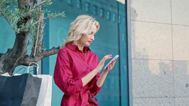 Una chica con paquetes está escribiendo sms después de ir de compras — Vídeo de stock