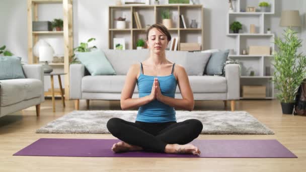 Mujer joven en posición de loto haciendo namaste en la sala de estar — Vídeo de stock