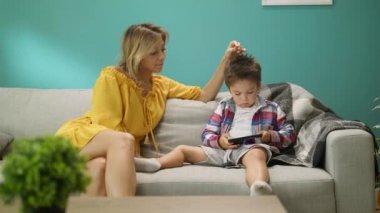 Annesi ile küçük çocuk oturma odasında kanepede bir akıllı telefon üzerinde bir oyun oynar