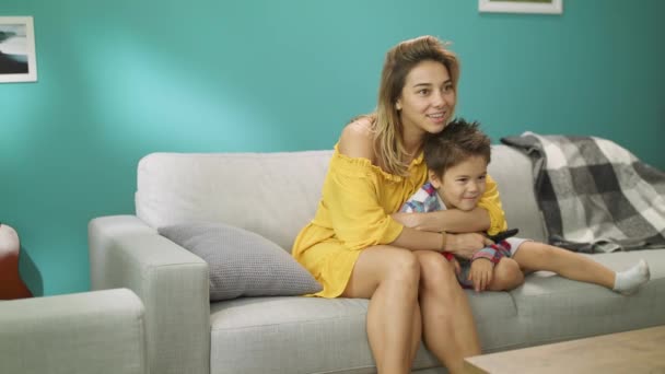 Mamá e hijo viendo la televisión mientras están sentados en un sofá en la sala de estar — Vídeos de Stock