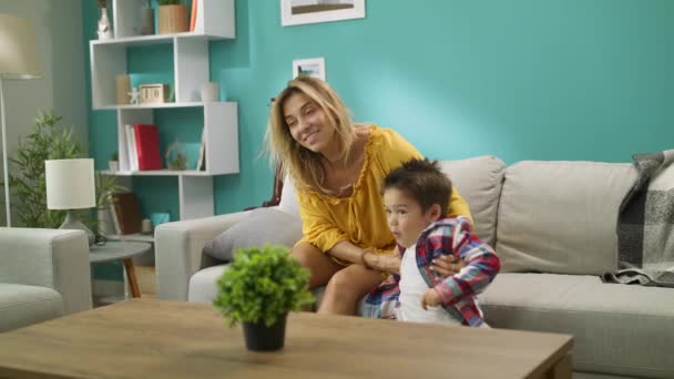 Mamá y su hijo viendo la televisión mientras están sentados en un sofá en la habitación — Vídeos de Stock