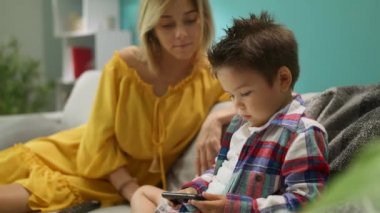 Anne ile küçük oğlu oturma odasında kanepede bir akıllı telefon üzerinde bir oyun oynar