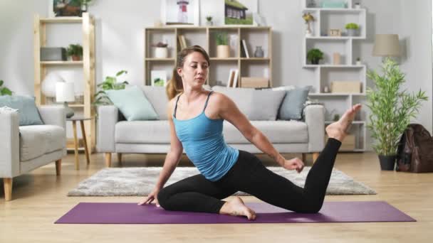 Joven mujer yoga estira las piernas, se dobla y se estira en casa — Vídeo de stock