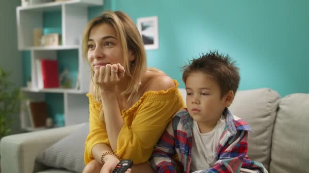 Mamma och son tittar på TV medan du sitter på en soffa i vardagsrummet — Stockvideo