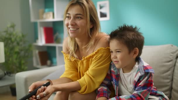 Happy child is watching TV with loving mother at home on couch — Stock Video