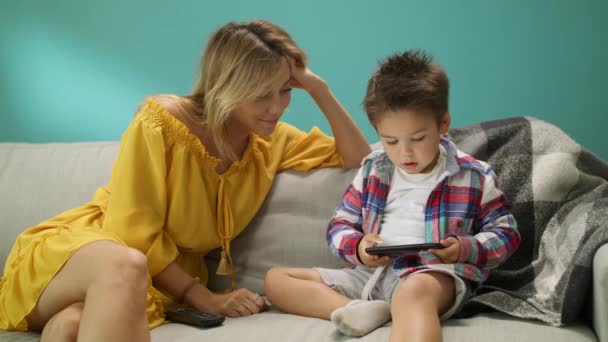 Menino com a mãe joga um jogo em um smartphone no sofá na sala de estar — Vídeo de Stock