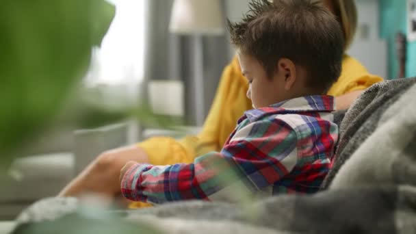Menino com a mãe joga um jogo em um smartphone no sofá na sala de estar — Vídeo de Stock