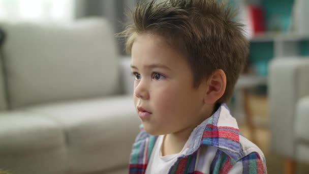 Маленький хлопчик уважно дивиться мультфільми по телевізору, сидячи на підлозі у вітальні — стокове відео