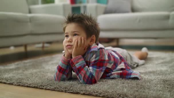 Мальчик внимательно смотрит мультики по телевизору, лежащие на полу в гостиной — стоковое видео