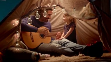 Babam çocuk çadırında küçük bir kız için gitar çalıyor.