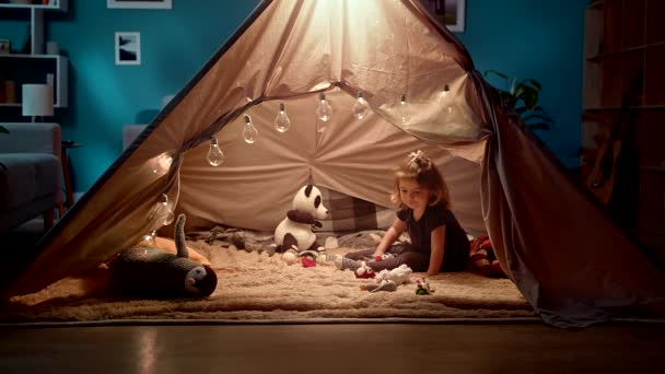 Menina brinca com brinquedos em uma tenda de brinquedo na sala — Vídeo de Stock