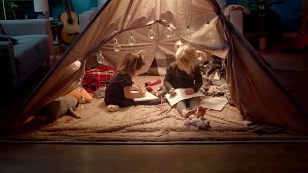 Medan små döttrar lokalisering i tält och ritning föräldrarna vilar på soffan — Stockvideo