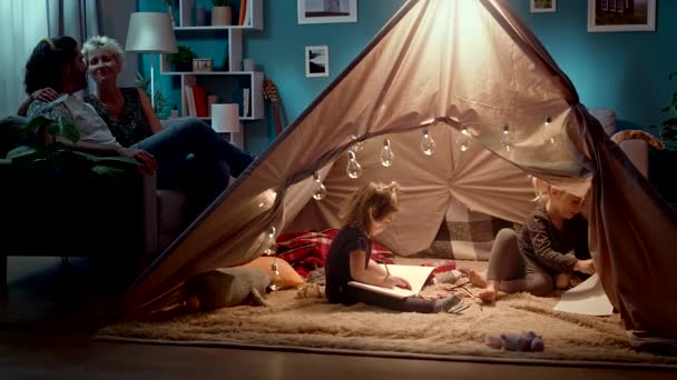 Küçük kızlar çadırda oturup ebeveynleri kanepeye çekiyorlar. — Stok video