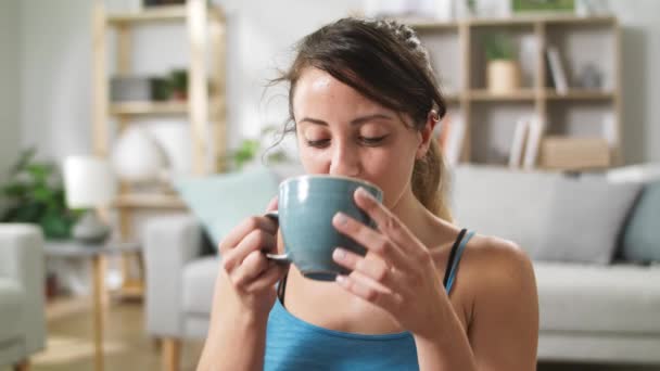 Mujer después de entrenar bebe agua de una taza mientras está sentado en el suelo — Vídeos de Stock