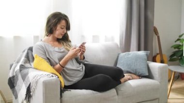 Oturma odasında kanepede bir telefon ile genç kadın