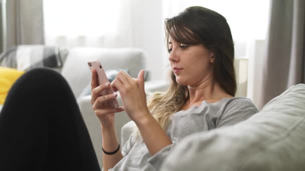 Genç kız rahat bir oturma odasında bir kanepede otururken bir telefon kullanır — Stok video