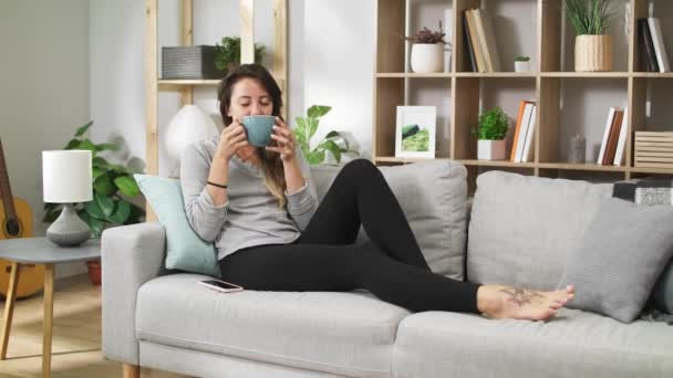 Mladá dívka pije čaj z velkého šálku v útulném obývacím pokoji — Stock video