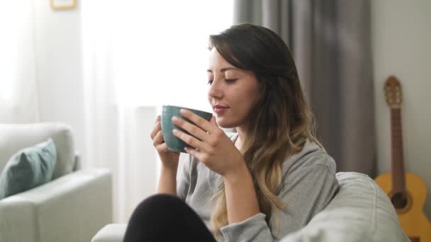 Chica joven bebe té de una taza grande en la sala de estar por la mañana — Vídeos de Stock