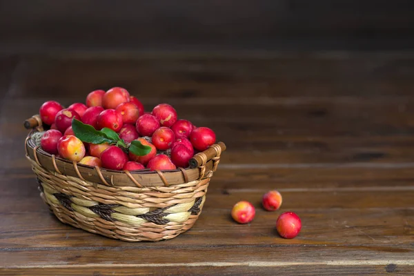 Red cherry plum in a straw basket on a wooden table — Stock Photo, Image