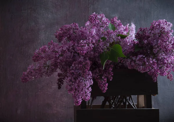 Bouquet of lilacs in a basket on a dark wooden background — Stock Photo, Image