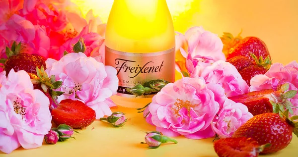 Uma garrafa de champanhe entre rosas e morangos. Fundo amarelo — Fotografia de Stock
