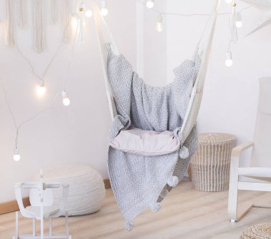 parlak bir odada rahat hamak sandalye. Pastel renkler. Gri yatak örtüsü. Ampuller bir çelenk