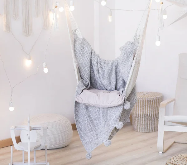 cozy hammock chair in a bright room. Pastel colors. Gray bedspread. A garland of light bulbs