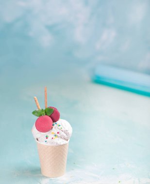 Mavi, turkuaz ve mor arka plan üzerinde bir kağıt fincan vanilyalı dondurma. Tatlılar ve dekoratif tatlı süslemeleri ile. Yan görünüm.