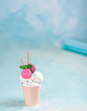 Mavi, turkuaz ve mor arka plan üzerinde bir kağıt fincan vanilyalı dondurma. Tatlılar ve dekoratif tatlı süslemeleri ile. Yan görünüm.