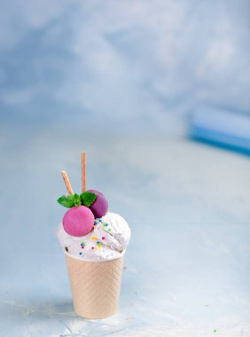 Mavi, turkuaz ve mor arka plan üzerinde bir kağıt fincan vanilyalı dondurma. Tatlılar ve dekoratif tatlı süslemeleri ile. Yan görünüm.