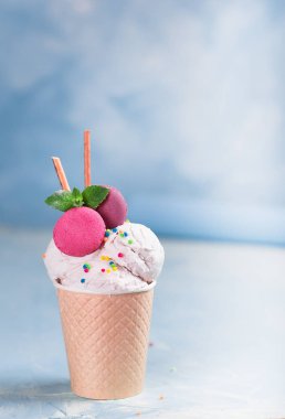 Mavi, turkuaz ve mor arka plan üzerinde bir kağıt fincan vanilyalı dondurma. Tatlılar ve dekoratif tatlı süslemeleri ile. Yan görünüm.