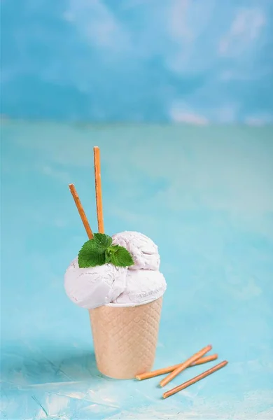 Vanilla ice cream in a paper cup on a blue, turquoise and purple background. With sweets and decorative sweet decorations. Side view. — Stock Photo, Image