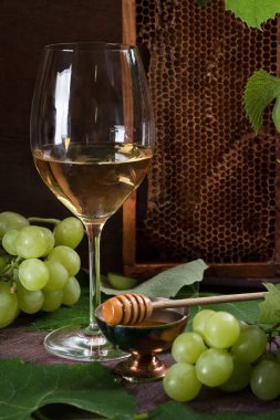 Bardakta beyaz şarap. Bardaklar üzüm yaprakları ve yeşil üzüm yanında koyu bir masa üzerinde durmak. Petek.