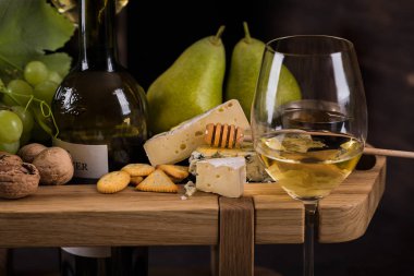 Peynir tabağı. Bir bardak beyaz şarap, peynir, bal, armut ve üzümle.