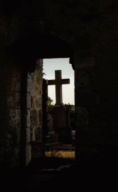 Ortaçağ mezarlığından bir taş haç silueti. Günbatımında bir mezarlığın kilisesinin kapısı tarafından çerçevelenmiş..