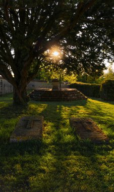 Eski bir ortaçağ mezarlığı. Mezar taşlarında haçlar var. Gün batımında bir ağacın altındaki yeşil çimenlikte..