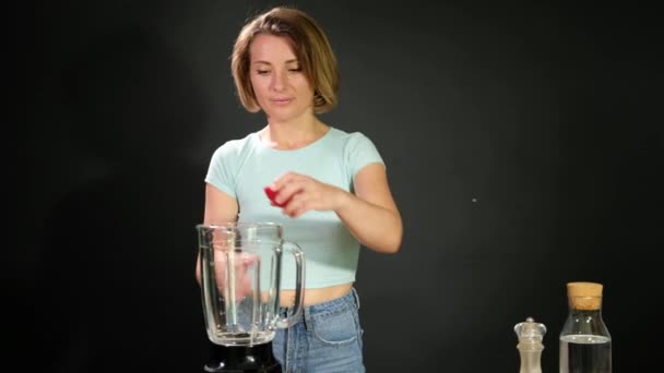 A young woman is cooking raw gazpacho. She puts tomatoes in the blender — Stock Video