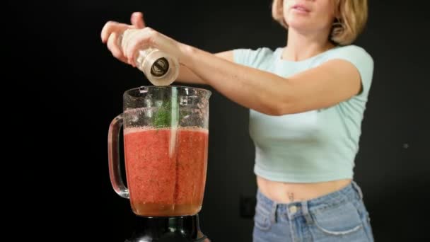 Een jonge vrouw kookt rauwe gazpacho. Ze voegt specerijen toe in een blender — Stockvideo